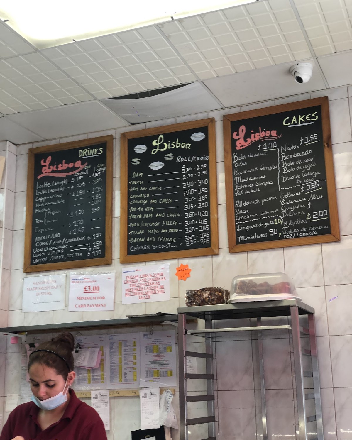 Staff serving behind the counter at Lisboa Patisserie, chalkboard menus above